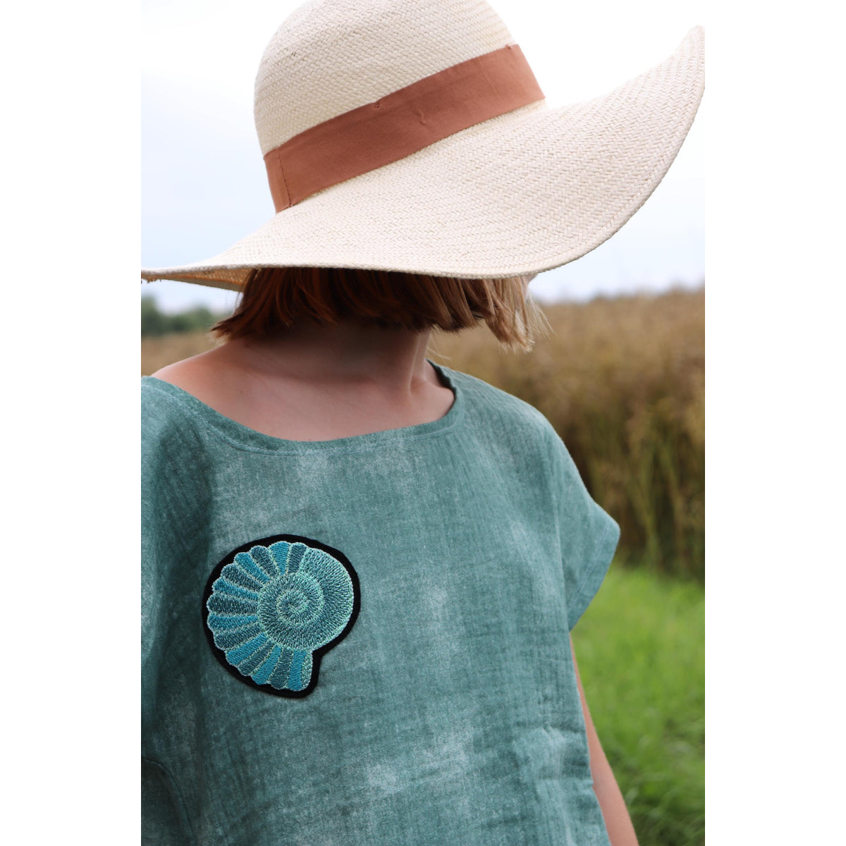 Maritime Applikations-Stickdatei – Kind mit Sonnenhut im petrolfarbenen Shirt mit Muschel-Applikation