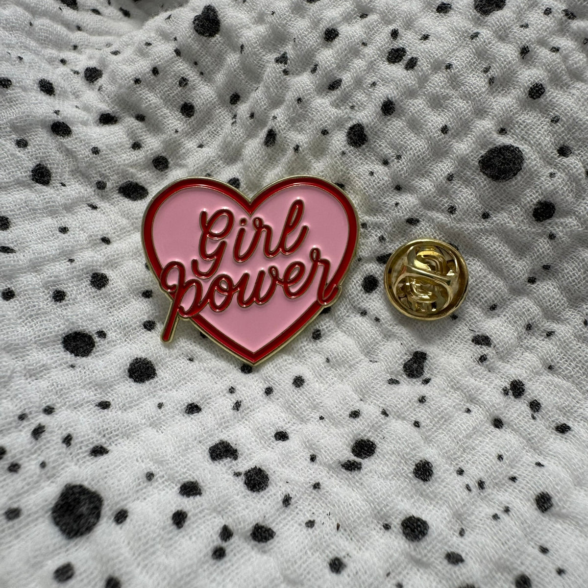 Emaille-Pin „Girl Power“ auf gepunktetem Stoff, daneben der Pin-Verschluss
