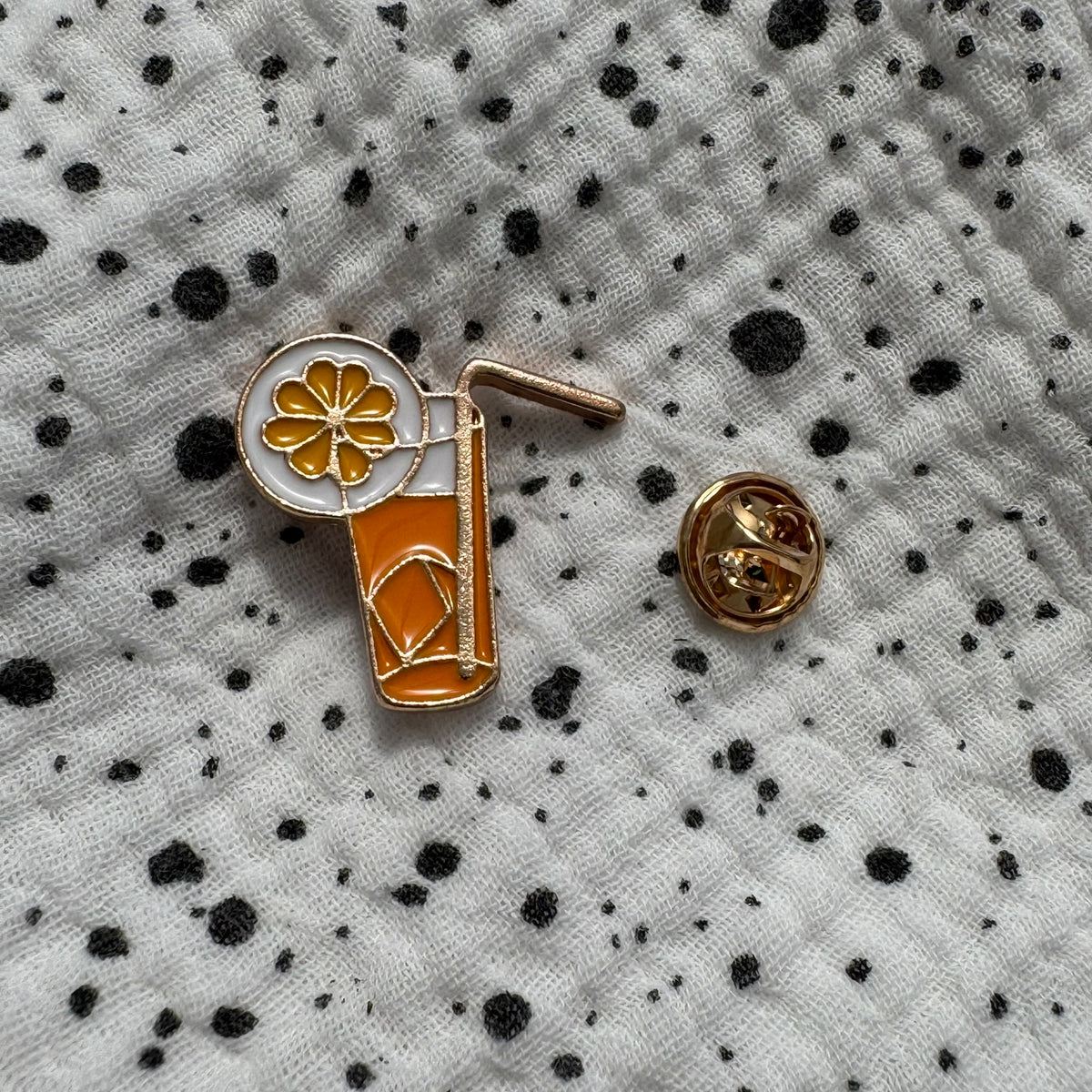 Emaille-Pin „Limonade“ auf gepunktetem Stoff, daneben der Pin-Verschluss
