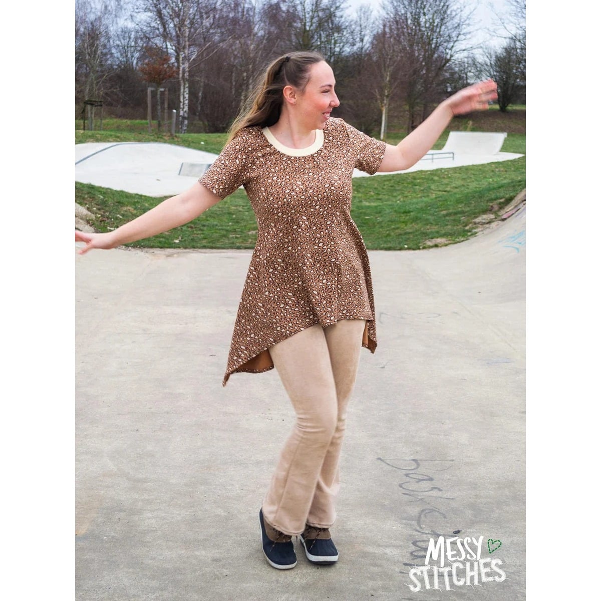 Sweet Mama Tunika Schnittmuster – Frau in brauner gemusterter Tunika mit Leggings auf einem Platz (genähtes Designbeispiel)