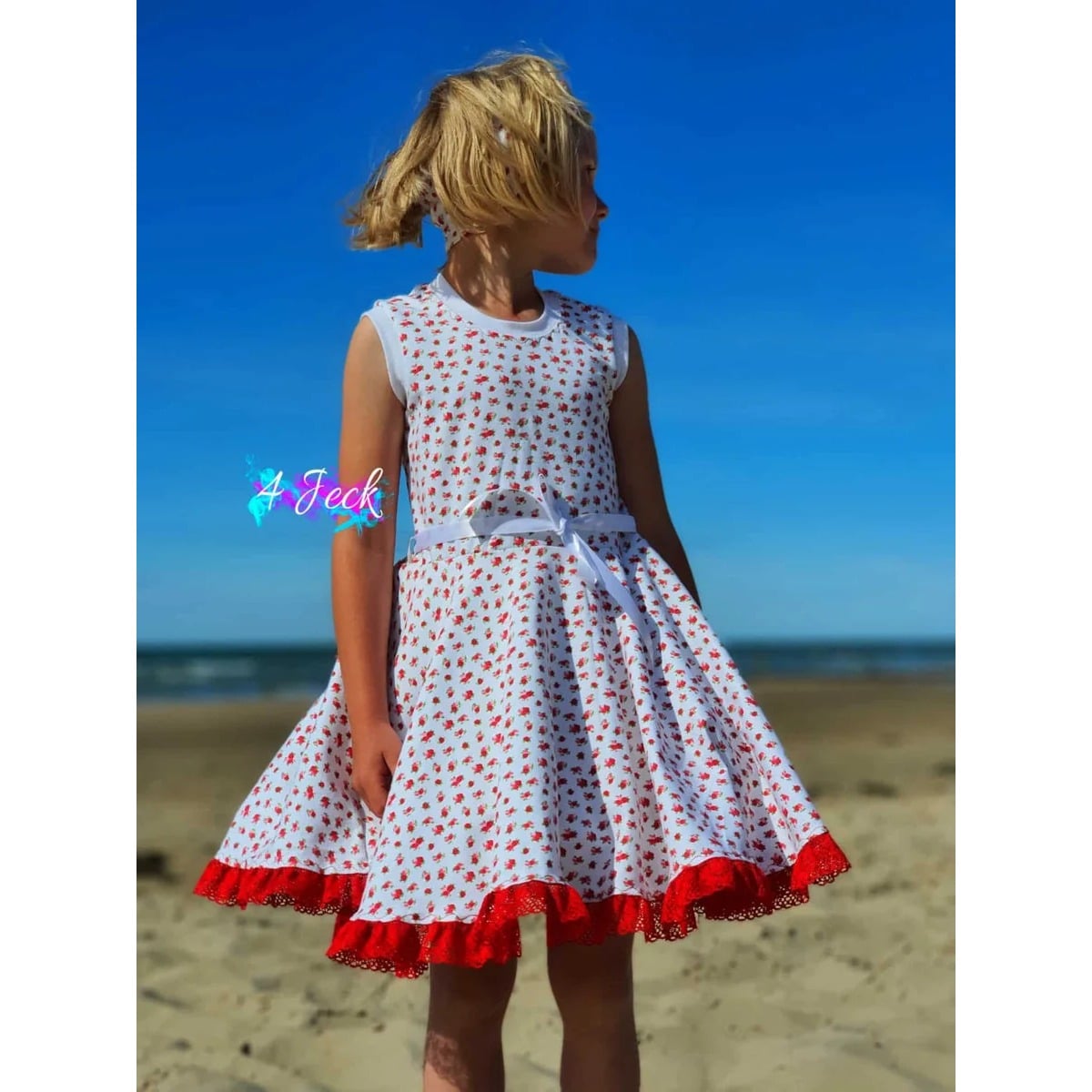 WinterDreams Kleid Schnittmuster – Mädchen im gepunkteten WinterDreams-Kleid mit rotem Saum am Strand (genähtes Designbeispiel)