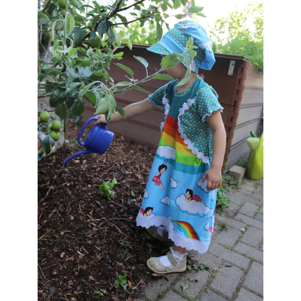 Kleid kleine Madame Schnittmuster – Mädchen im Regenbogen-Kleid im Garten, Seitenansicht (genähtes Designbeispiel)