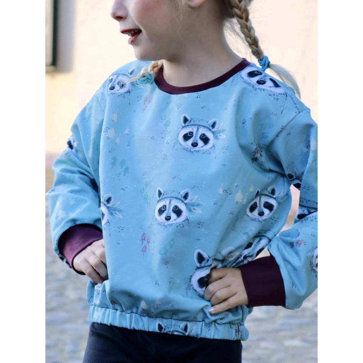 Oversized Pulli Schnittmuster – Kind im hellblauen Oversized-Pulli mit Waschbär-Motiv (genähtes Designbeispiel)