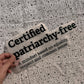 Bügelbild Certified patriarchy-free groß in Schwarz, ca. 30,5 x 13,5 cm, in der Hand gehalten