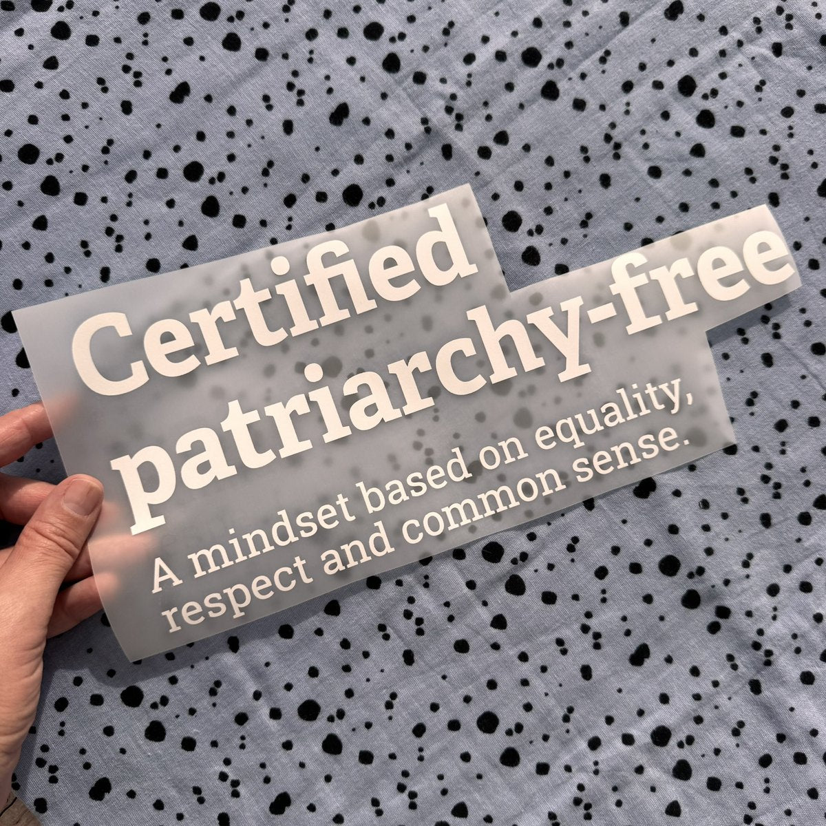 Bügelbild Certified patriarchy-free groß in Weiß, ca. 30,5 x 13,5 cm, in der Hand gehalten