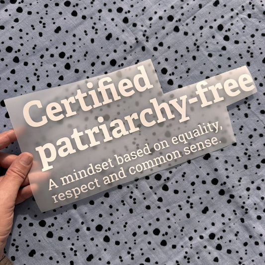 Bügelbild Certified patriarchy-free groß in Weiß, ca. 30,5 x 13,5 cm, in der Hand gehalten