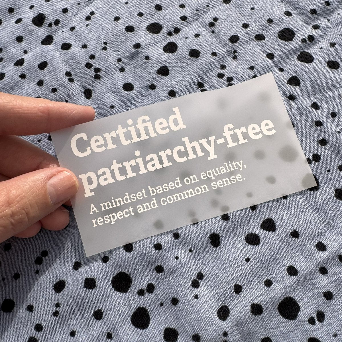 Bügelbild Certified patriarchy-free klein in Weiß, ca. 10 x 4,5 cm, in der Hand gehalten