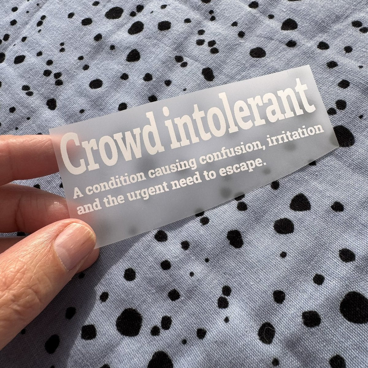 Bügelbild Crowd intolerant klein in Weiß, ca. 10 x 3 cm, in der Hand gehalten