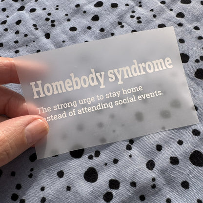 Bügelbild Homebody syndrome klein in Weiß, ca. 9,5 x 3 cm, in der Hand gehalten