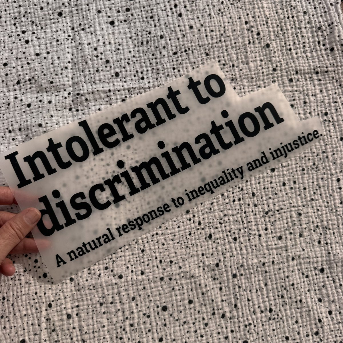 Bügelbild Intolerant to discrimination groß in Schwarz, ca. 32 x 13 cm, in der Hand gehalten