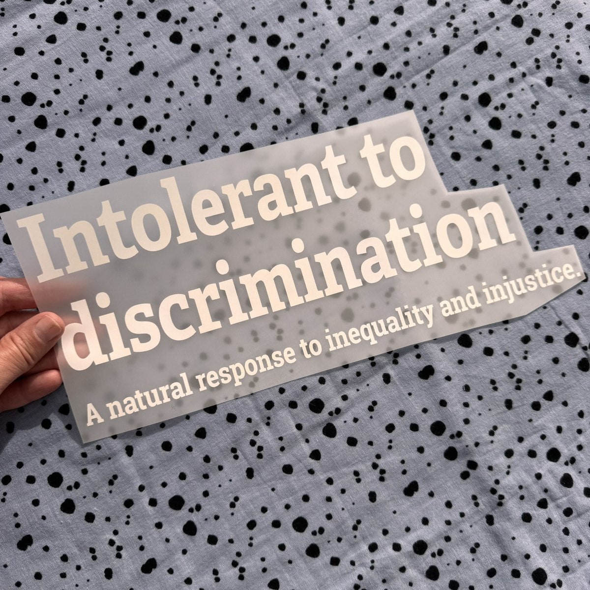 Bügelbild Intolerant to discrimination groß in Weiß, ca. 32 x 13 cm, in der Hand gehalten