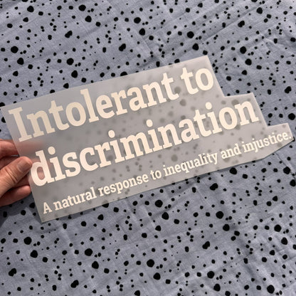Bügelbild Intolerant to discrimination groß in Weiß, ca. 32 x 13 cm, in der Hand gehalten