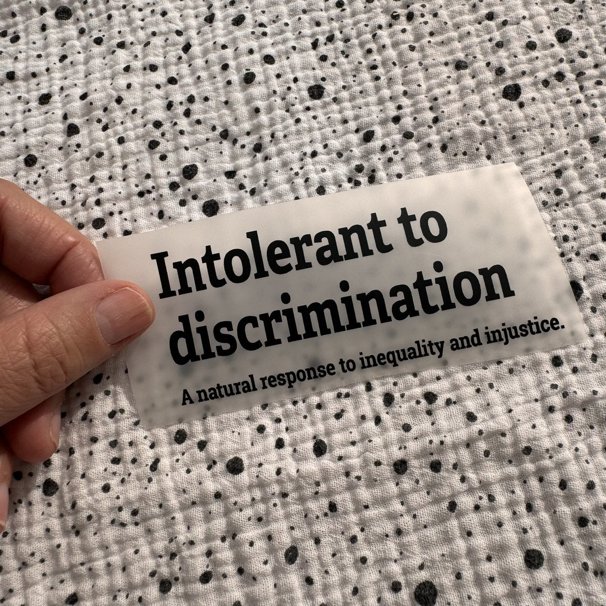 Bügelbild Intolerant to discrimination klein in Schwarz, ca. 10,5 x 4,5 cm, in der Hand gehalten