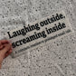 Bügelbild Laughing outside, screaming inside groß in Schwarz, ca. 29,5 x 11,5 cm, in der Hand gehalten