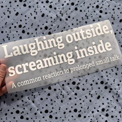 Bügelbild Laughing outside, screaming inside groß in Weiß, ca. 29,5 x 11,5 cm, in der Hand gehalten