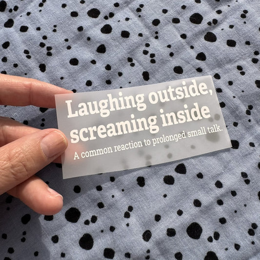 Bügelbild Laughing outside, screaming inside klein in Weiß, ca. 10 x 4 cm, in der Hand gehalten