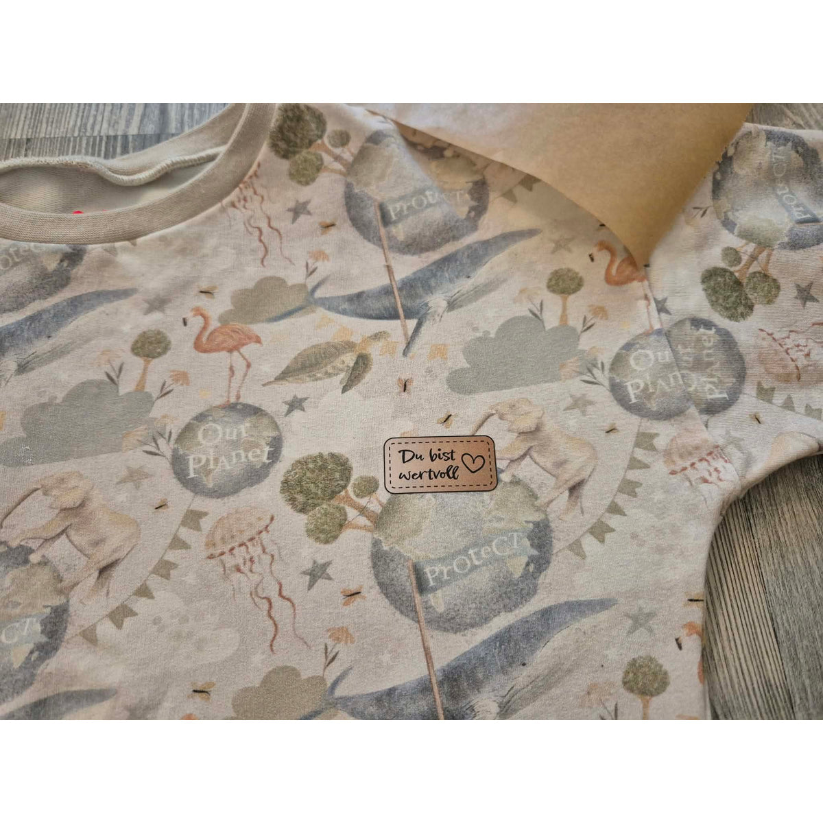 Bügelbild Wertvolle Label – Label „Du bist wertvoll“ mit Herz auf einem Pulli mit Planeten-, Wal- und Flamingo-Print, Nahaufnahme (Beispielbild)