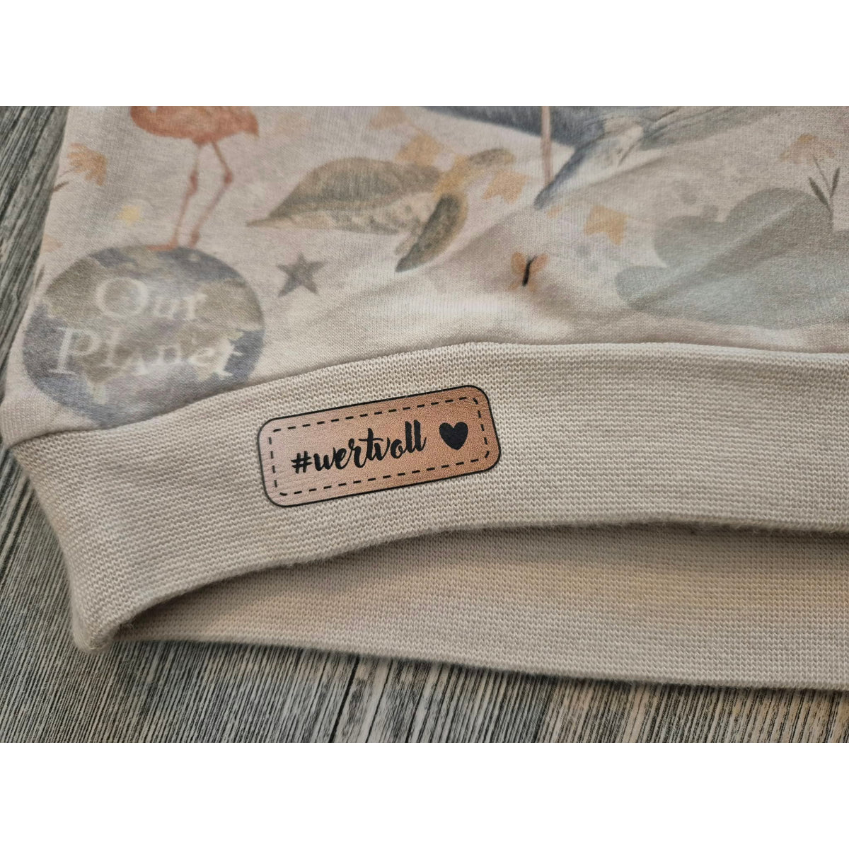Bügelbild Wertvolle Label – Label „#wertvoll“ mit Herz auf dem beigen Bündchen eines Pullis (Beispielbild)