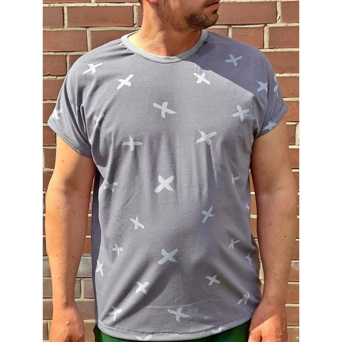 Mann im grauen Family Shirt Herren mit weißem Kreuz-Muster und angenähtem Ärmelumschlag vor Backsteinwand