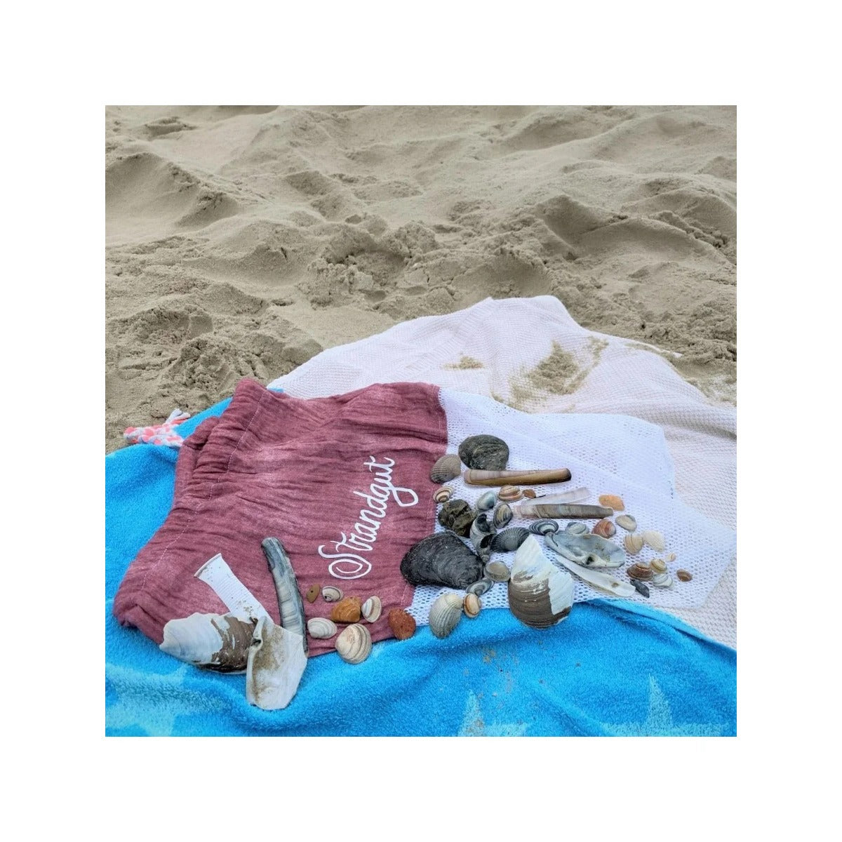Freebook Sammelbeutel Strandgut – beerenfarbener Netzbeutel mit Schriftzug Strandgut (aus der passenden Plotterdateiserie mit diesem Namen) und gesammelten Muscheln am Strand