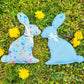 Hasensilhouette Freebie – zwei hellblaue Stoffhasen mit Ostermotiven im Gras zwischen Löwenzahn