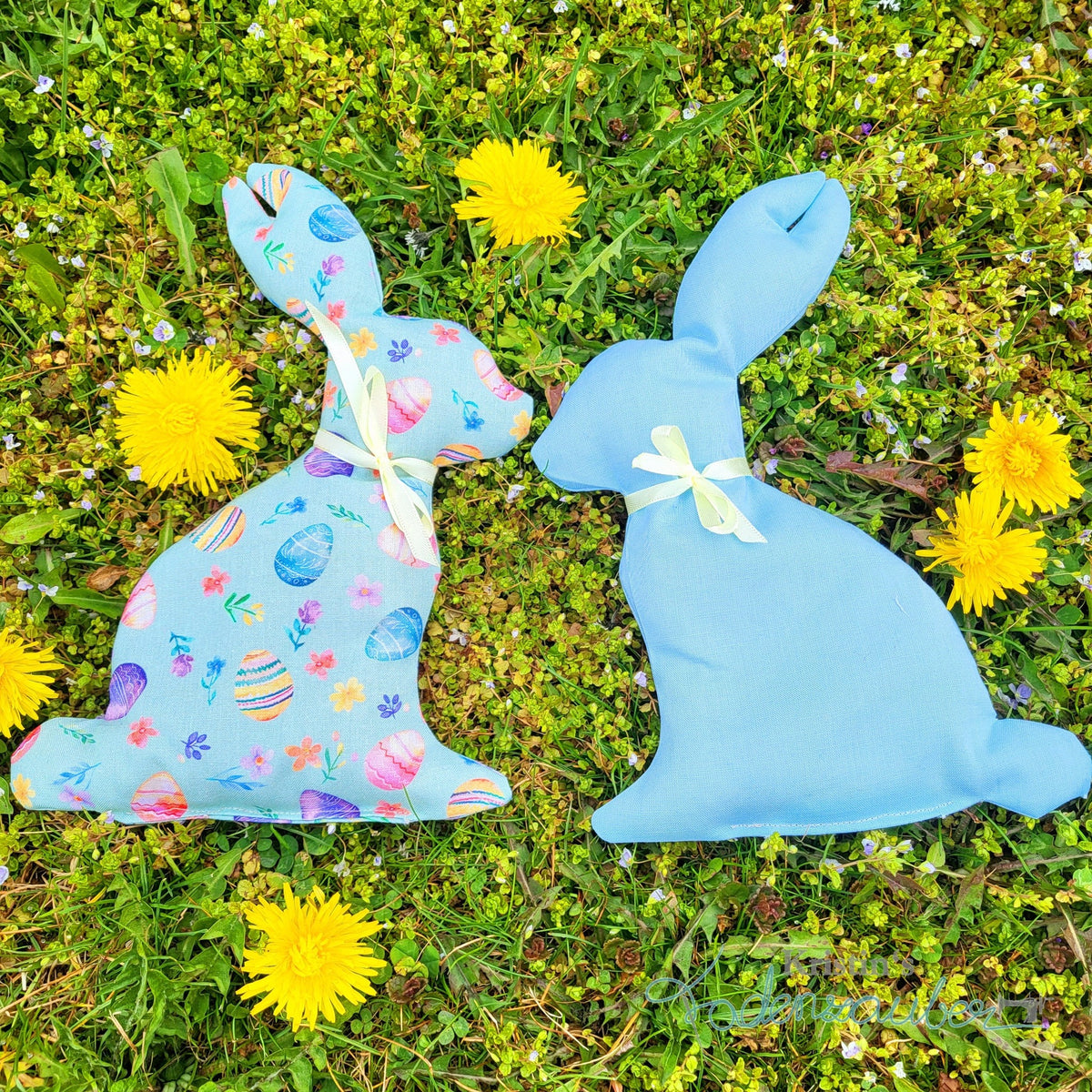 Hasensilhouette Freebie – zwei hellblaue Stoffhasen mit Ostermotiven im Gras zwischen Löwenzahn