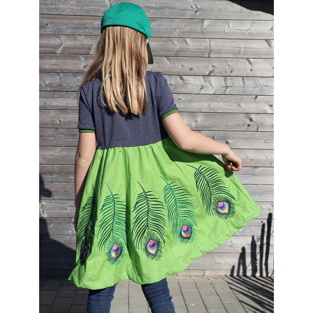 Lottis Drehkleid Schnittmuster – Rückansicht mit jeansfarbenem Oberteil und grünem Bahnenrockteilen mit bestickten Pfauenfedern