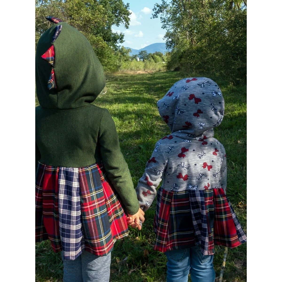 Lottis Drehkleid Schnittmuster – zwei Kinder von hinten, grünes Drachen-Drehkleid mit eingenähten Zacken an der Kapuze und graues Kleid mit Schleifen, beide mit Karo-Rock