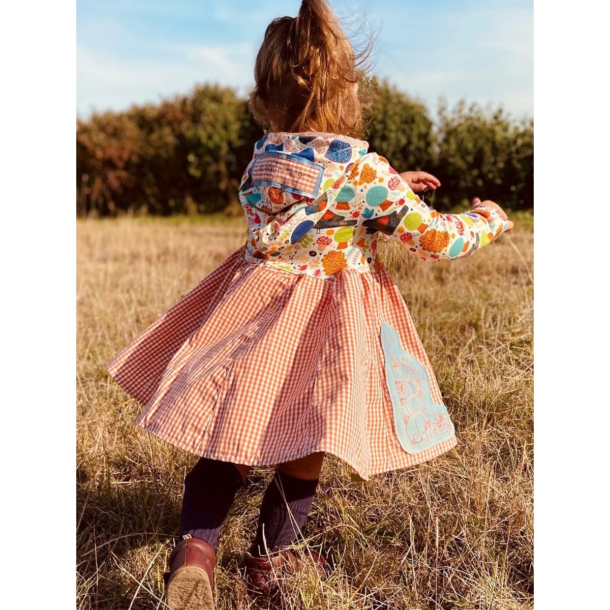 Lottis Drehkleid Schnittmuster – Mädchen im Herbstkleid mit Kapuze, Vogel-Blätter-Print und orangem Karo-Rock mit Kürbis-Plotterdatei
