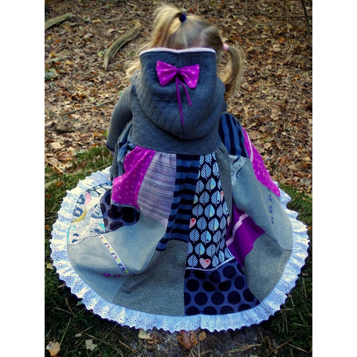 Lottis Drehkleid Schnittmuster – Rückansicht mit grauer Steppkapuze und Oberteil aus dem selben Steppstoff, pinker Schleife und Patchworkrock mit weißer Lochspitze