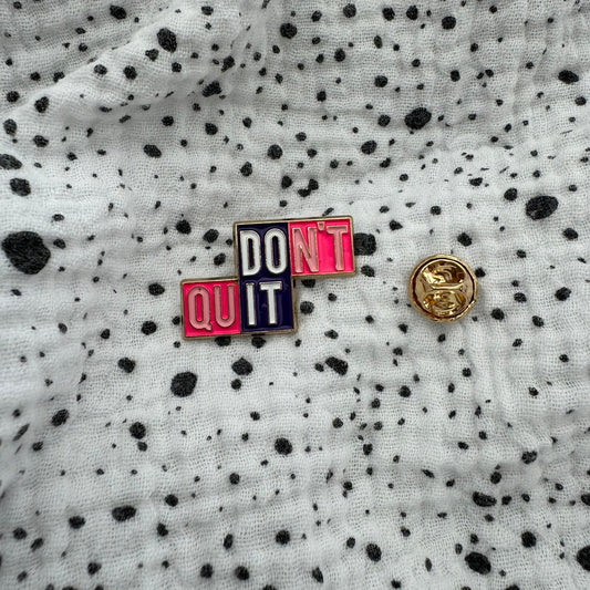 Emaille-Pin „Don’t quit – DO IT“ auf gepunktetem Stoff, daneben der Pin-Verschluss