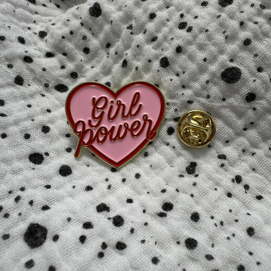 Emaille-Pin „Girl Power“ auf gepunktetem Stoff, daneben der Pin-Verschluss