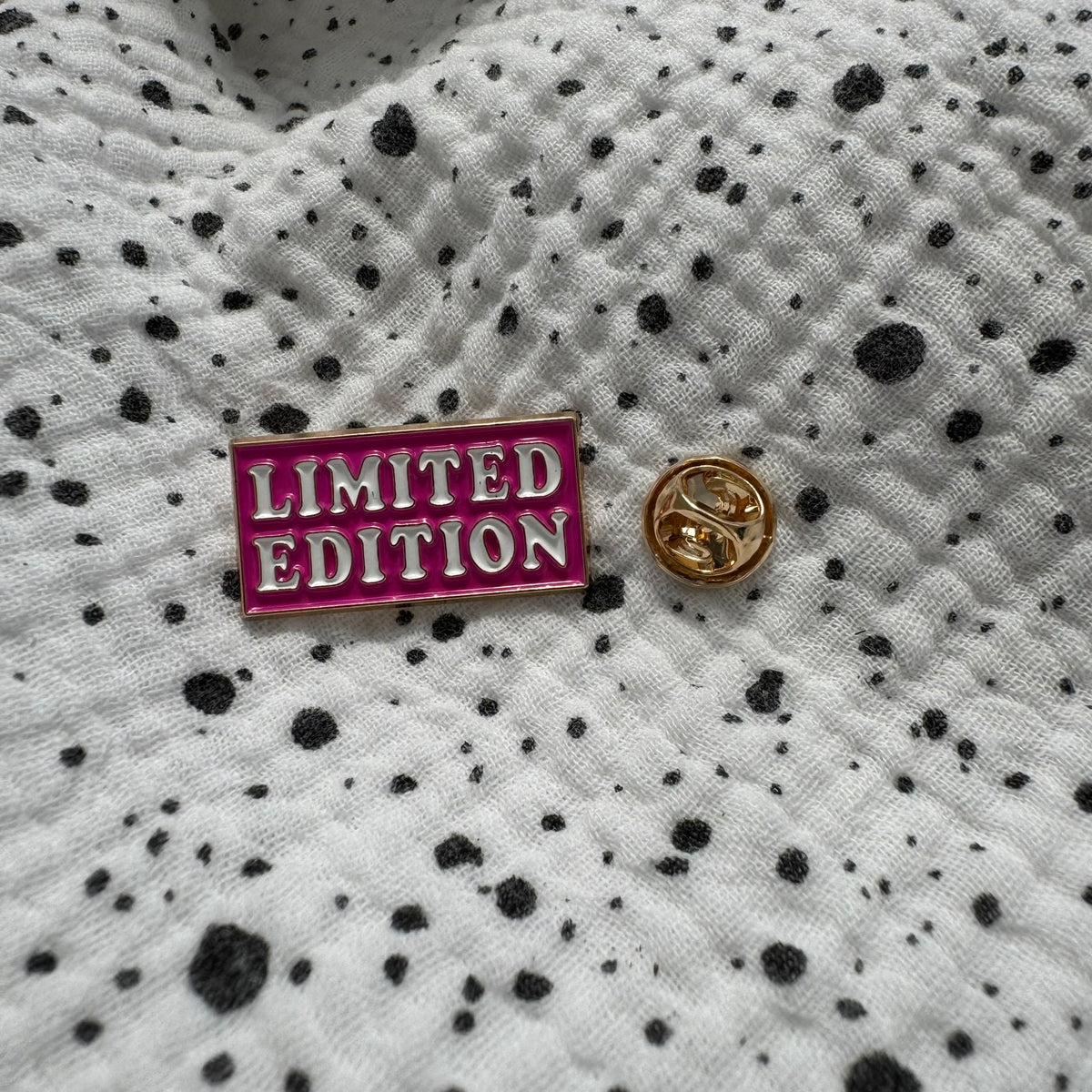 Emaille-Pin „Limited Edition“ auf gepunktetem Stoff, daneben der Pin-Verschluss