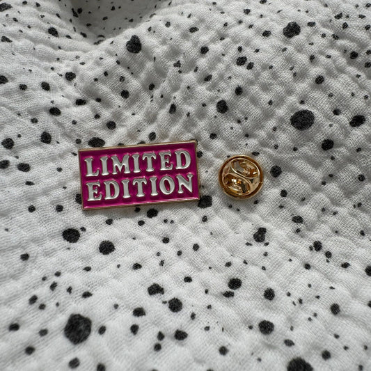 Emaille-Pin „Limited Edition“ auf gepunktetem Stoff, daneben der Pin-Verschluss
