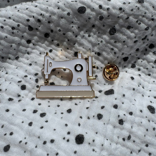 Emaille-Pin „Nähmaschine“ auf gepunktetem Stoff, daneben der Pin-Verschluss