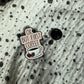 Emaille-Pin „OK, but first coffee“ auf gepunktetem Stoff, daneben der Pin-Verschluss