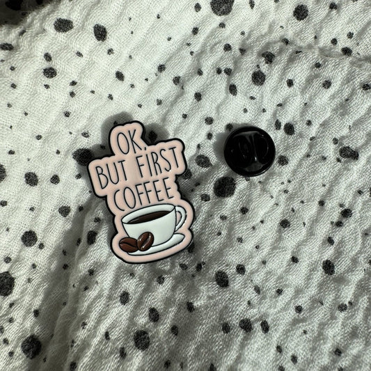 Emaille-Pin „OK, but first coffee“ auf gepunktetem Stoff, daneben der Pin-Verschluss