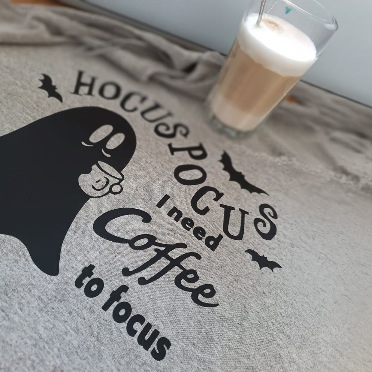 Coffee Ghosts Plotterdatei – „Hocus Pocus, I need coffee to focus“ schwarz auf einem grau melierten Shirt, daneben ein Latte macchiato