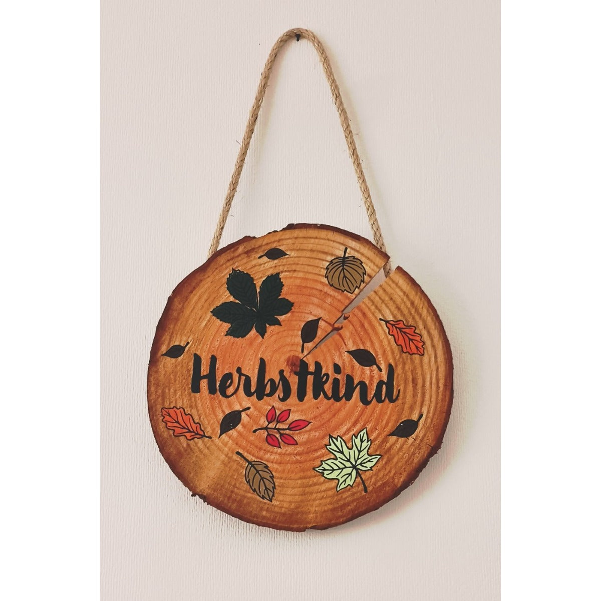 Herbstkind Plotterdatei – schwarzer Schriftzug mit bunten Blättern auf einer Holzscheibe mit Kordel als Wanddeko