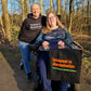 Intolerant Club Plotterdatei – Statement „Intolerant to discrimination“ auf schwarzem Hoodie und auf einer Stofftasche in Orange und Grün, zwei Frauen im Wald, eine im Rollstuhl