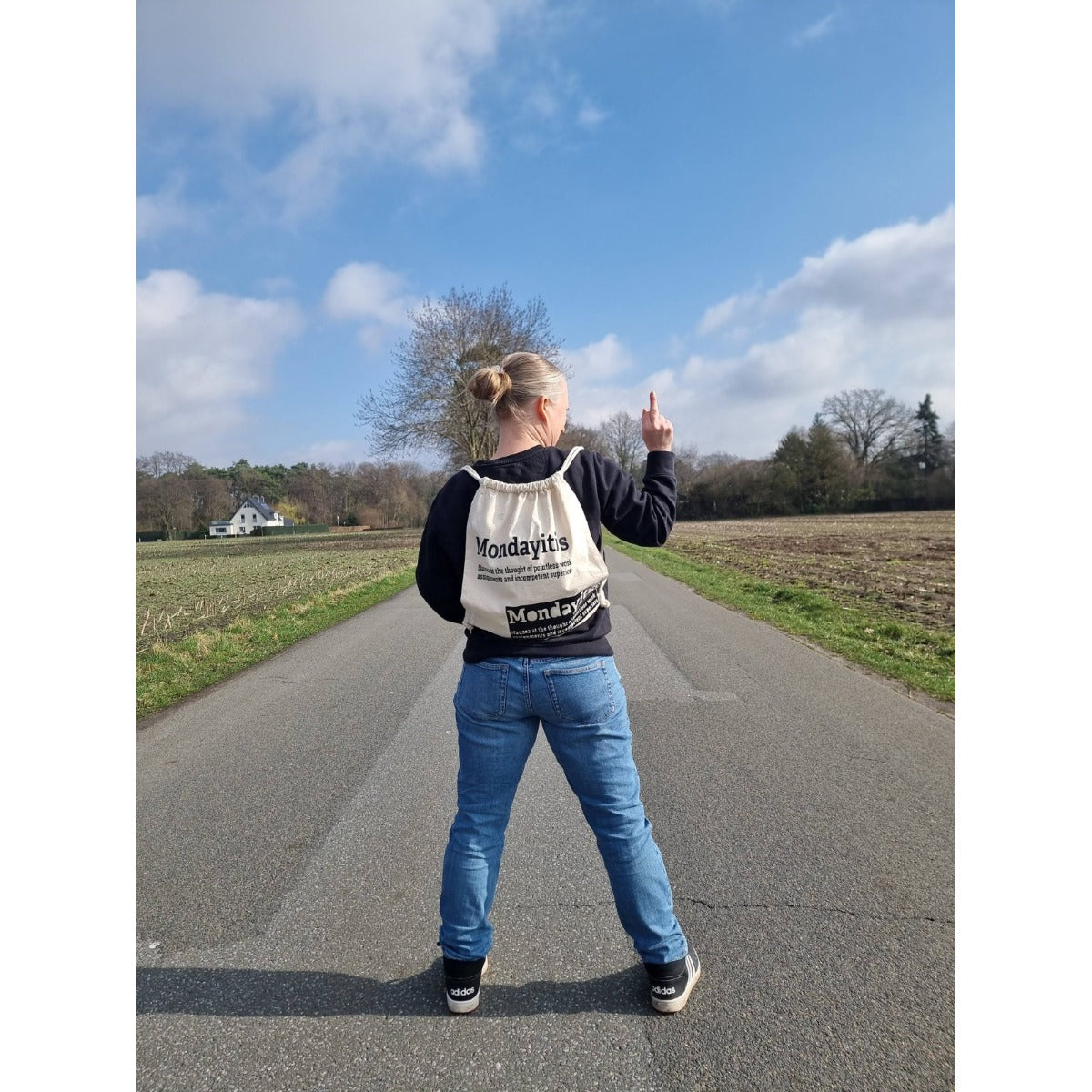 Intolerant Club Plotterdatei – Statement „Mondayitis“ schwarz auf einem naturfarbenen Turnbeutel, Frau von hinten auf einem Feldweg