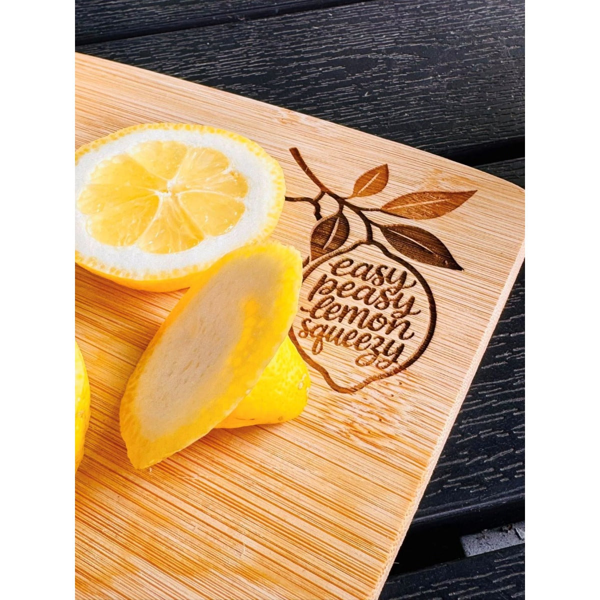 Lemon Squeezy als Lasergravur – Schneidebrett aus Holz mit dem Schriftzug Easy Peasy Lemon Squeezy in Zitronenform, daneben frische Zitronenscheiben