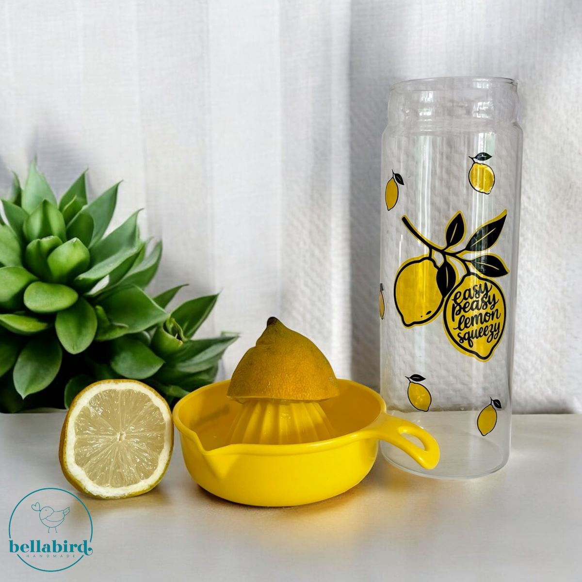 Glasflasche mit Zitronenmotiven und Schriftzug Easy Peasy Lemon Squeezy neben einer gelben Zitronenpresse
