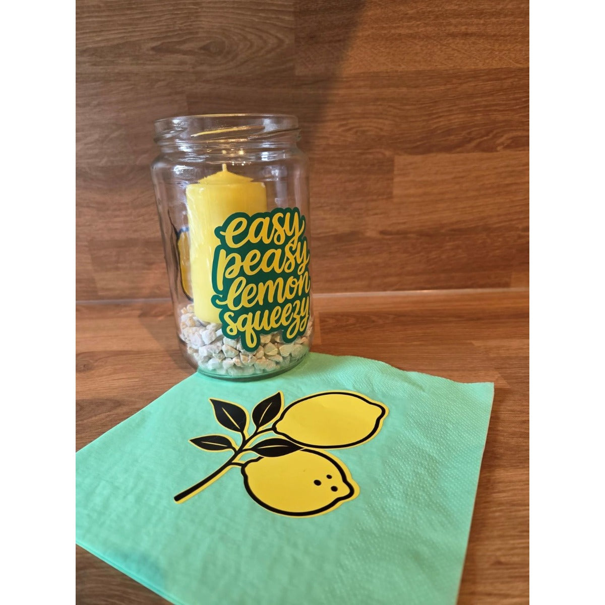 Windlicht aus einem Einmachglas mit dem Schriftzug Easy Peasy Lemon Squeezy in Grün, gelbe Kerze und Serviette mit Zitronenmotiv
