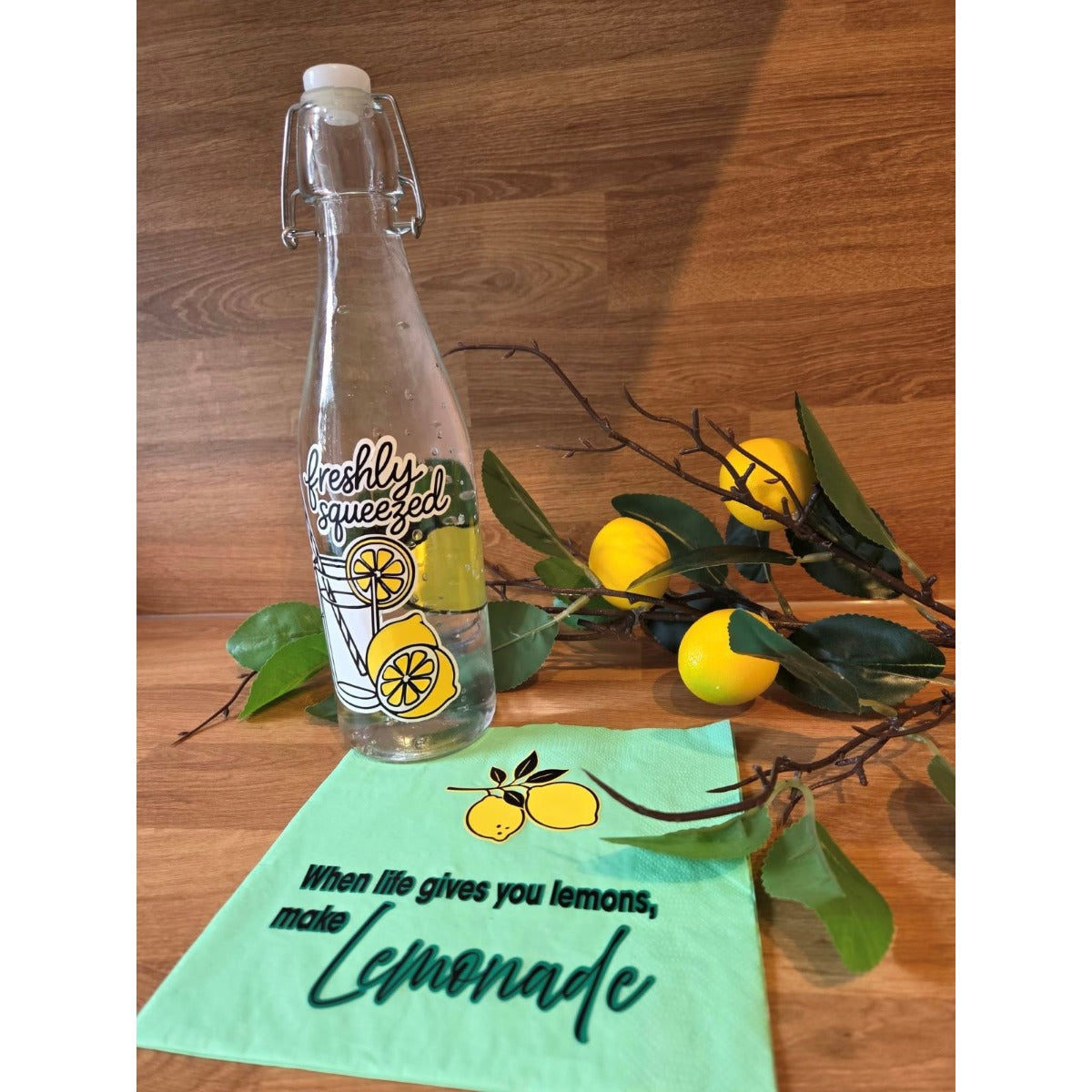 Bügelflasche mit dem Motiv Freshly Squeezed, daneben eine Serviette mit dem Spruch When life gives you lemons, make lemonade und ein Zitronenzweig