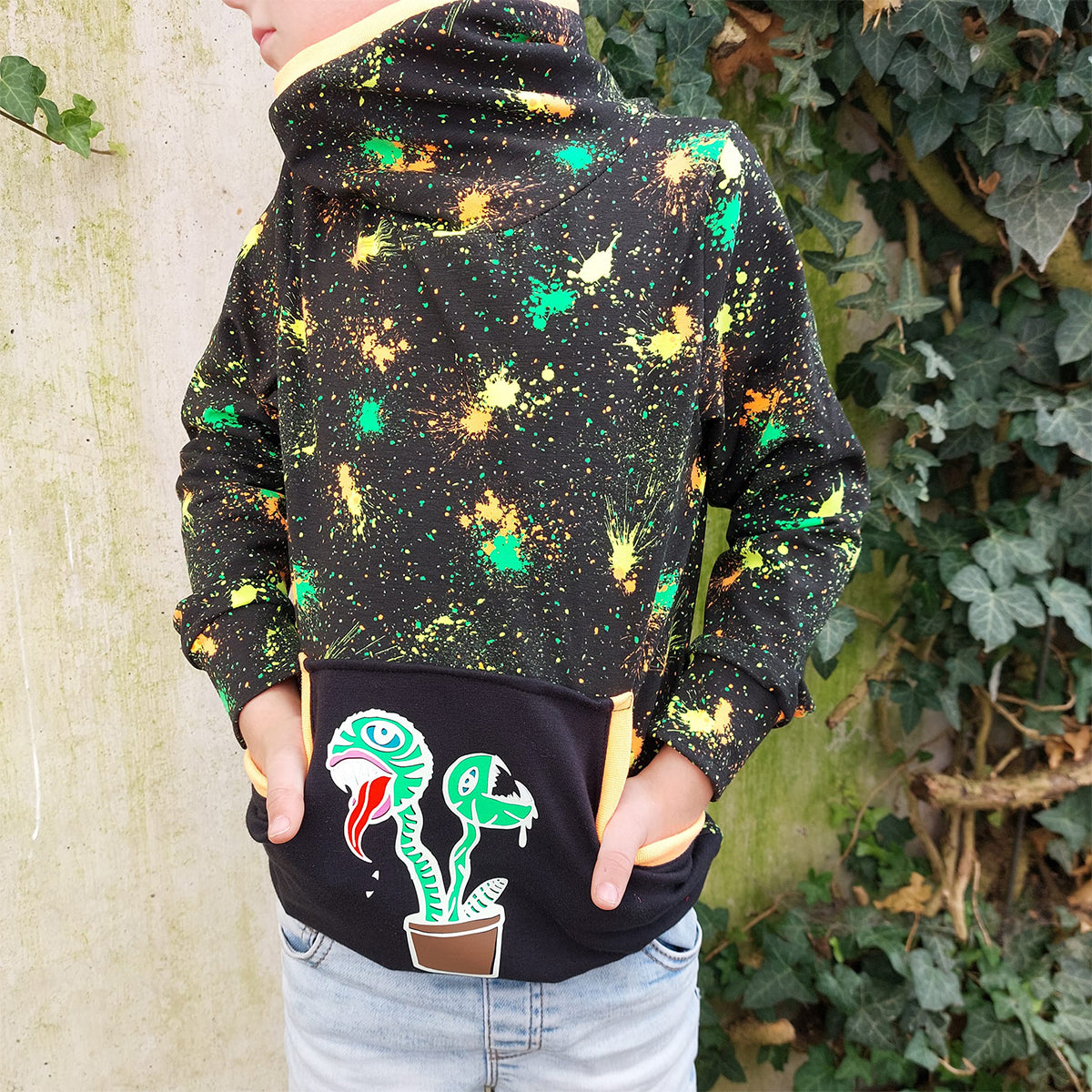 Plotterdatei Lottis Halloween Pflanzen – bunte Pflanzen auf der schwarzen Kängurutasche eines neonbunt gesprenkelten Hoodies