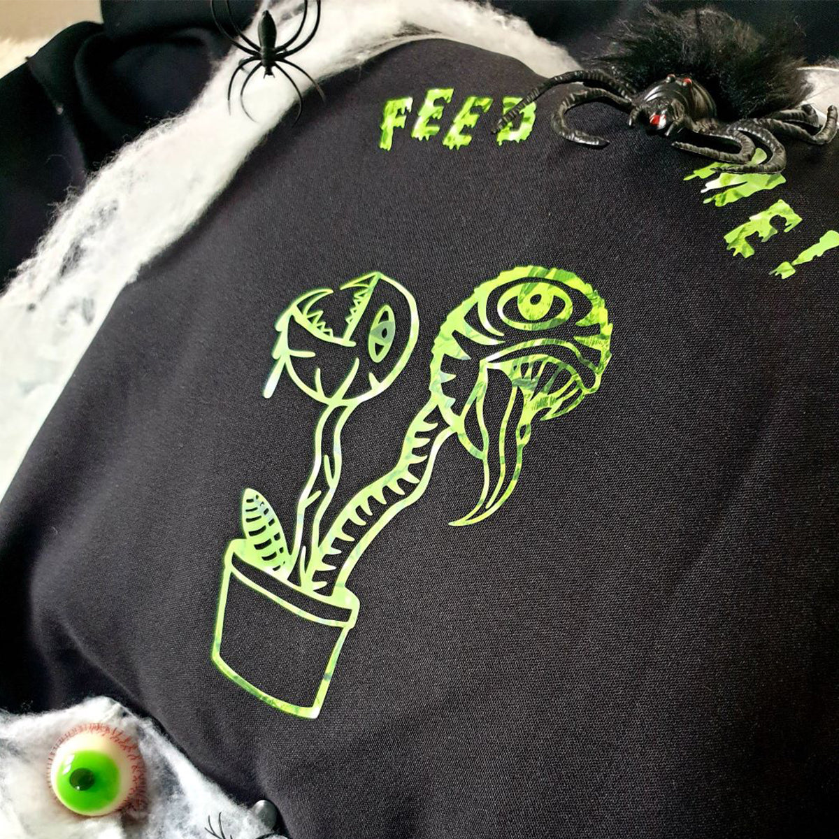 Plotterdatei Lottis Halloween Pflanzen – schwarzes Shirt mit grünem Pflanzenmotiv und FEED-ME-Schriftzug, dekoriert mit Spinnen und Glupschauge
