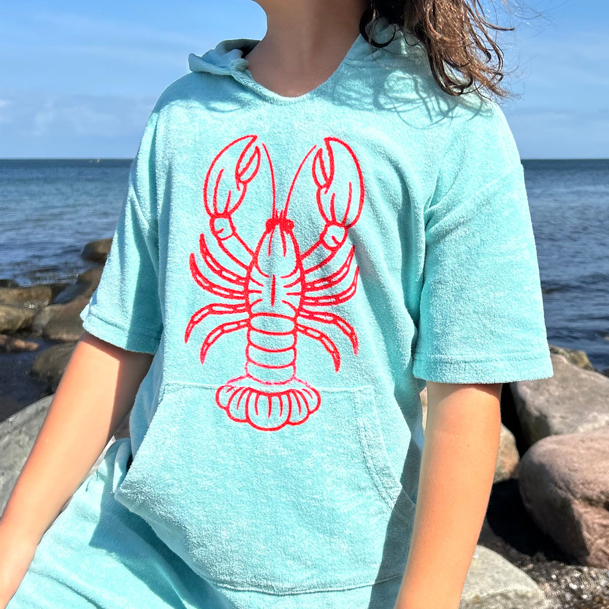 Mädchen im mintfarbenen Frottee-Hoodie mit rotem Hummer der Plotterdatei Sea Life am Meer