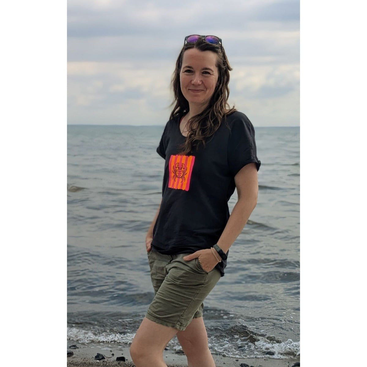 Frau im schwarzen T-Shirt am Meer mit Krebs der Plotterdatei Sea Life auf pink-orangen Streifen