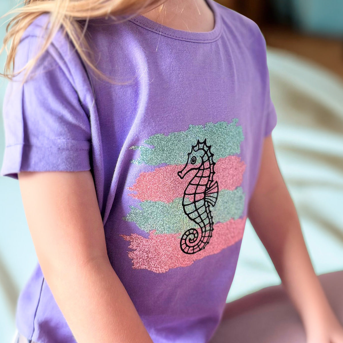 Mädchen im lila T-Shirt mit Seepferdchen der Plotterdatei Sea Life auf pastelliger Glitzerfolie